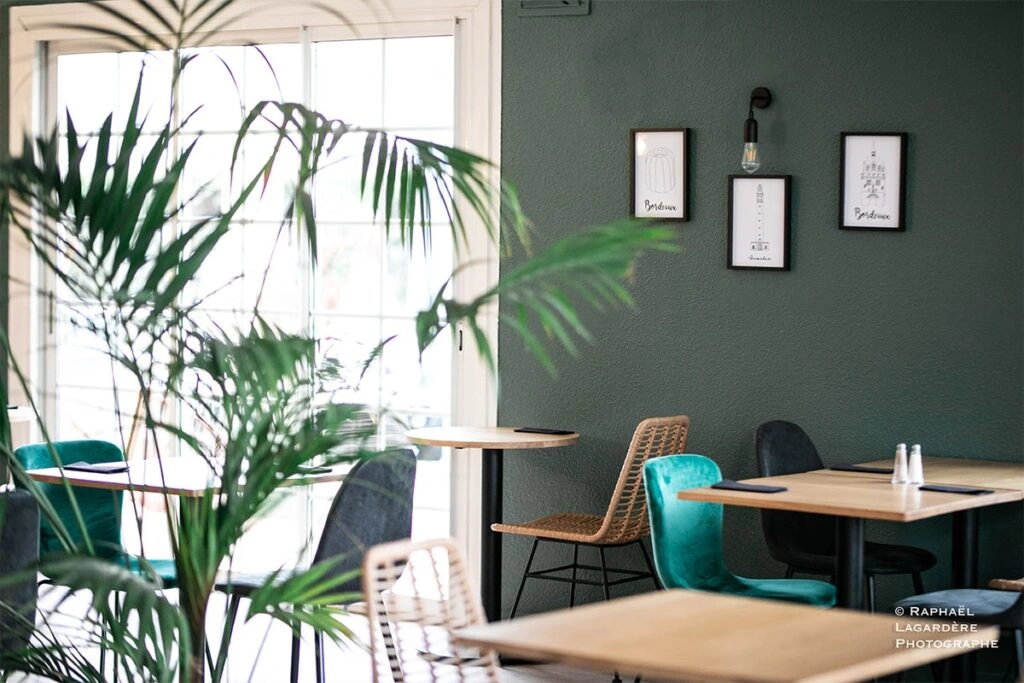 Zona de restaurante y salón del Hôtel Porte du Bassin, con plantas, sillas modernas y un ambiente cálido y acogedor.